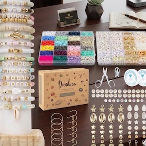 Puede incluir: Un kit para hacer joyer&iacute;a que incluye un soporte blanco con m&uacute;ltiples pulseras de cuentas, dos organizadores de pl&aacute;stico transparente con cuentas de arcilla y met&aacute;licas, una caja de cart&oacute;n con la etiqueta Deinduser, tijeras, cord&oacute;n el&aacute;stico y dijes.