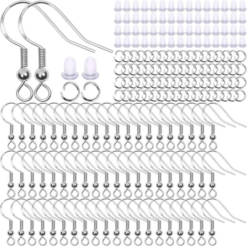 May include: A collection of silver-toned metal earring hooks featuring a coiled spring and a small bead detail, accompanied by numerous clear silicone earring backs and small circular metal jump rings for jewelry making and crafting projects.
