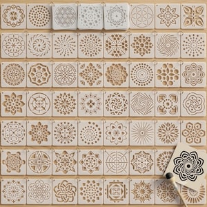 May include: A collection of square white plastic stencils featuring various intricate geometric and floral mandala patterns. Each stencil has a small hole in the corner for organization, and one stencil is shown with a black painted design.