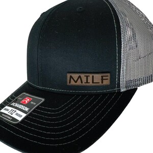 May include: Black and grey trucker hat with a brown leather patch that says "MILF" on the front.