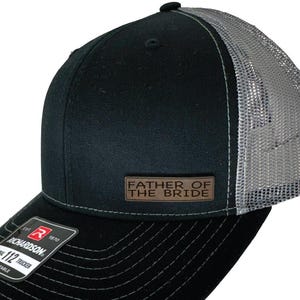 May include: Black and grey trucker hat with a brown leather patch that says "Father of the Bride".