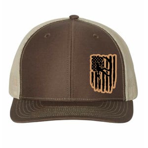 May include: Brown and tan trucker hat with a brown bill and a mesh back. The hat features a distressed American flag design with a silhouette of a rock climber.