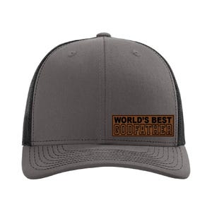 May include: A gray and black trucker hat with a brown patch that reads "WORLD'S BEST GODFATHER".