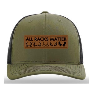May include: A green and black trucker hat with a brown leather patch that reads "ALL RACKS MATTER" with a series of antlers and a bra graphic.