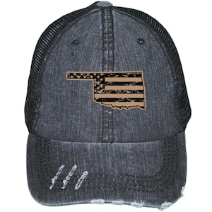 May include: A black distressed denim trucker hat with a mesh back. The hat features a distressed American flag design in the shape of the state of Oklahoma.