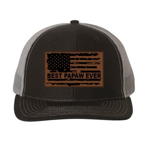 May include: A black and gray trucker hat with a brown patch featuring a distressed American flag and the text "BEST PAPAW EVER".