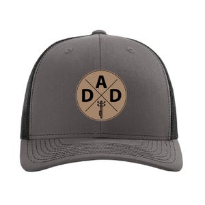May include: A gray trucker hat with a black mesh back. The hat has a brown circle patch with the letters "A D D" and a stylized image of a power line.