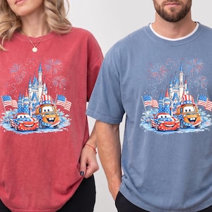 A woman wearing a red t-shirt with a graphic of a castle and fireworks, and a man wearing a blue t-shirt with a graphic of a castle and fireworks.