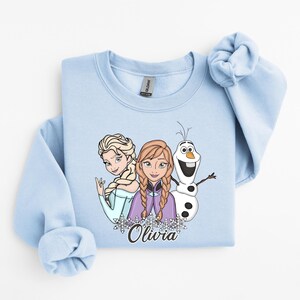 A light blue sweatshirt with a graphic design featuring two cartoon characters and a snowman.