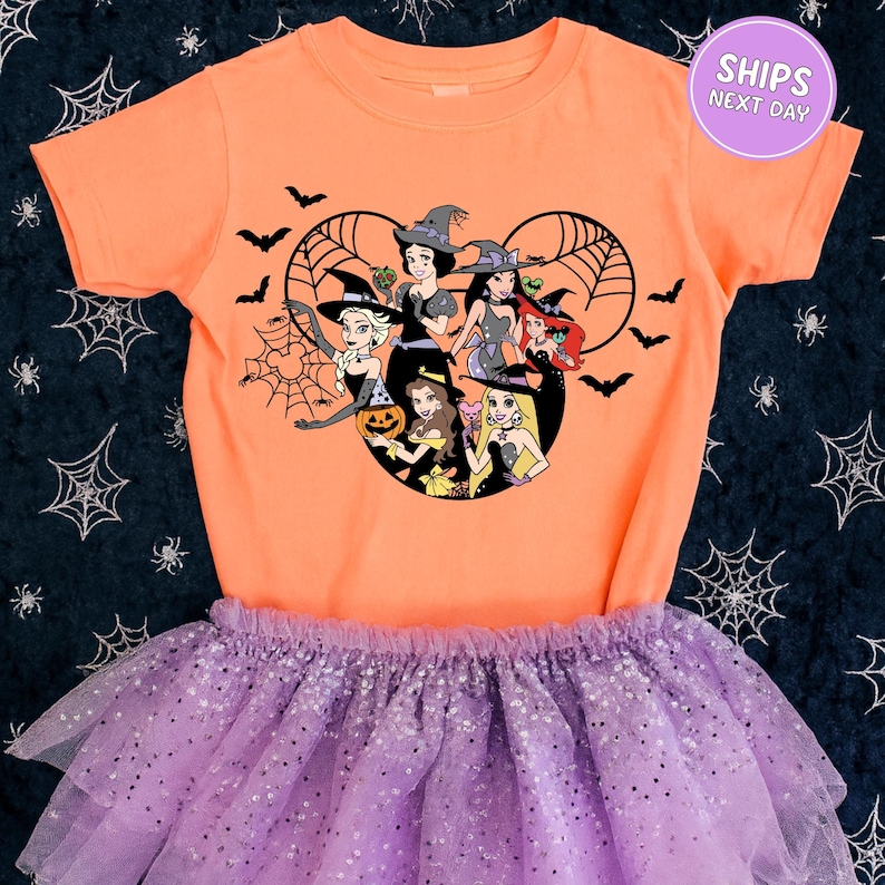 A children's orange t-shirt with a Halloween-themed graphic of Disney princesses and a purple tutu skirt.