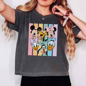 A woman wearing a gray t-shirt with a graphic of Disney characters Mickey Mouse, Minnie Mouse, Goofy, Donald Duck, and Pluto.
