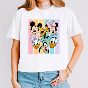 A woman wearing a white t-shirt with a colorful graphic of Disney characters on it.