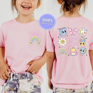A young girl wearing a pink t-shirt with various cartoon-style illustrations and text on the back.