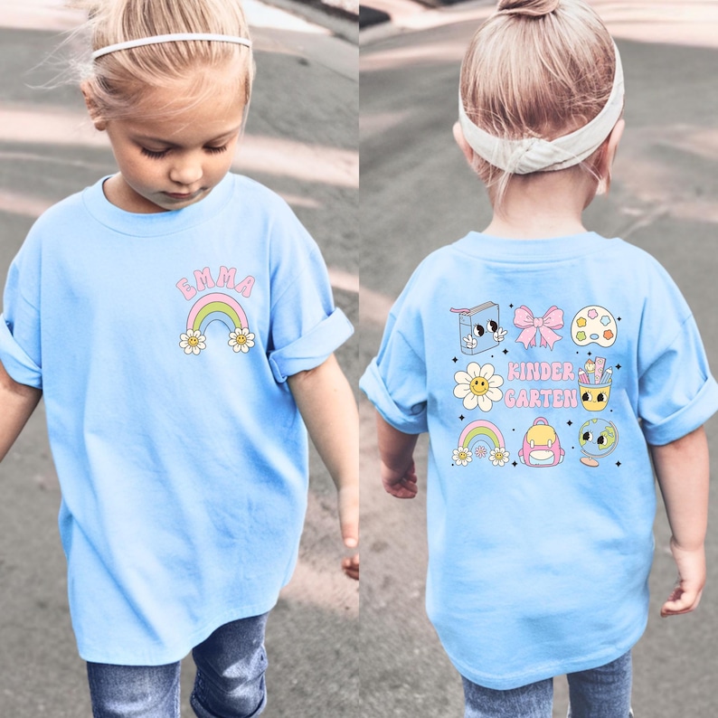 A young girl wearing a blue t-shirt with a rainbow and cartoon characters on the back, walking on a street.