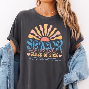 A woman wearing a black t-shirt with a graphic design that says "SUNSET CLASS OF 2026" and a sun-like design.