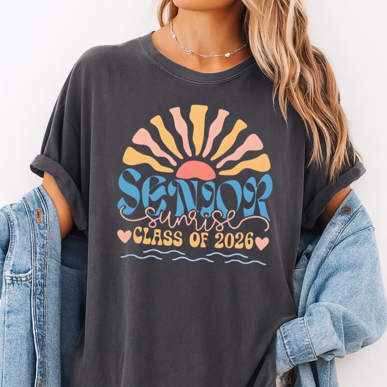 A woman wearing a black t-shirt with a graphic design that says "SUNSET CLASS OF 2026" and a sun-like design.