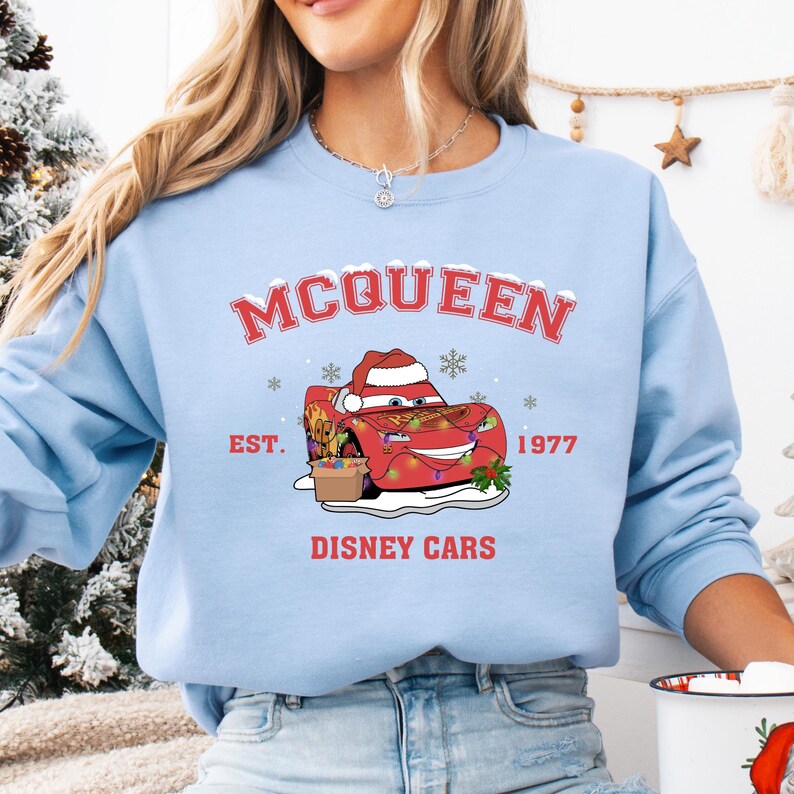 A woman wearing a light blue sweatshirt with a graphic of a red car and the text "McQueen" and "Disney Cars" printed on it.