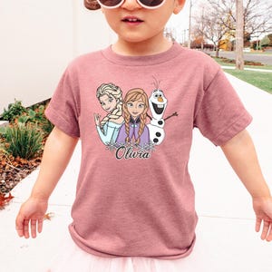 A young girl wearing a pink t-shirt with a graphic of characters from the Disney movie Frozen.