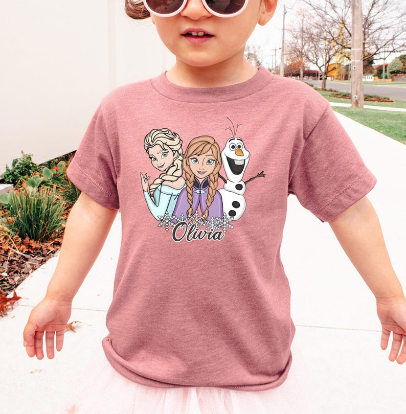 A young girl wearing a pink t-shirt with a graphic of characters from the Disney movie Frozen.
