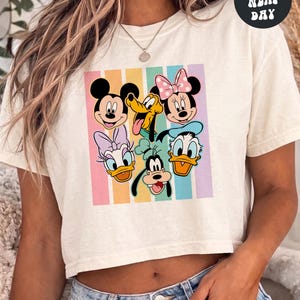 A woman wearing a white crop top with a graphic of Disney characters on it.
