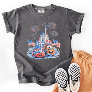 A gray t-shirt with a graphic of a castle and fireworks, along with a pair of checkered shoes, is displayed on a white background.