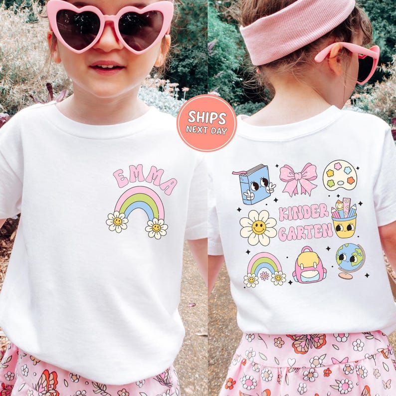 A young girl wearing a white t-shirt with a colorful, cartoon-style design and pink heart-shaped sunglasses.