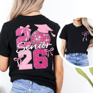 A woman wearing a black t-shirt with a pink and black design that says "2016 Senior" and features a graduation cap, a disco ball, and a ribbon.
