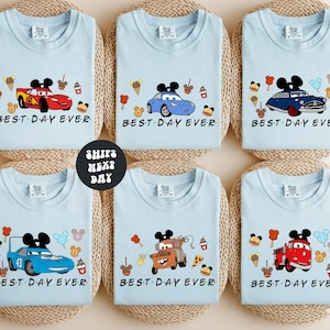 six identical light blue t-shirts with the phrase "BEST DAY EVER" printed on them, featuring various Disney characters and vehicles.
