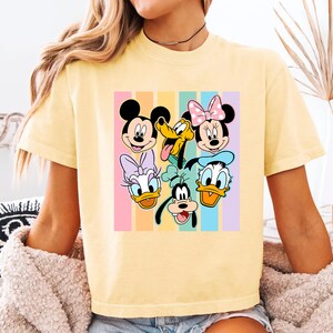 A yellow t-shirt with a colorful graphic of Disney characters such as Minnie Mouse, Mickey Mouse, Donald Duck, Goofy, and Pluto.