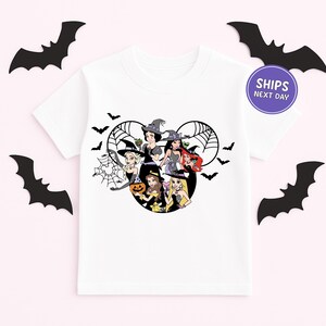 A white t-shirt with a graphic design featuring cartoon characters, including a witch, a pumpkin, and other Halloween-themed figures, surrounded by bats.