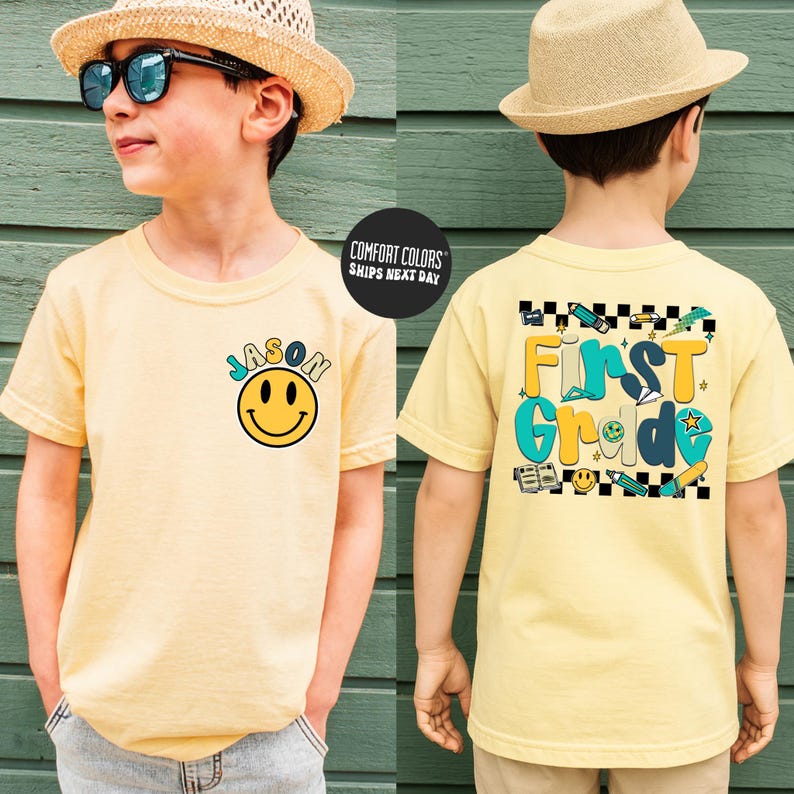 A young boy wearing a yellow t-shirt with a smiley face and text, standing in front of a green wall.