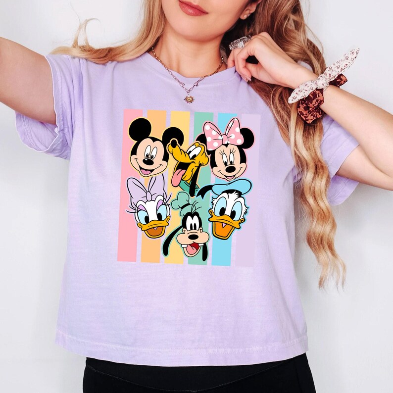 A woman wearing a purple t-shirt with a graphic of Disney characters Mickey Mouse, Minnie Mouse, Goofy, Donald Duck, and Pluto.