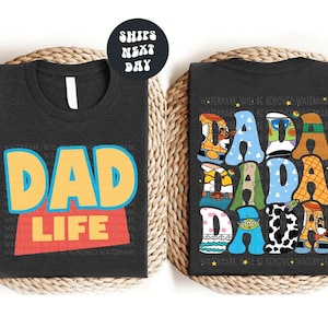 two t-shirts with the text "DAD LIFE" printed on them. The t-shirt on the left has the text "DAD LIFE" in a bold, colorful font, while the t-shirt on the right has the text "DAD LIFE" in a more playful, cartoon-like font. The t-shirts are placed on a woven mat, and there is a note indicating that the t-shirts are available in t-shirt, sweathirt, and long sleeve options.