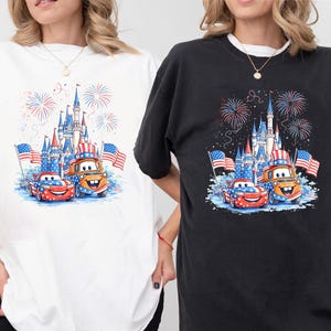 two people wearing t-shirts with a graphic design depicting a castle, fireworks, and two cartoon cars.