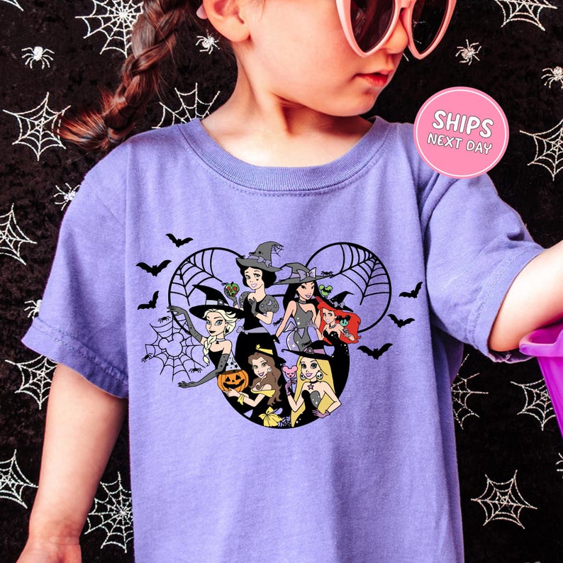 A young girl wearing a purple t-shirt with a Halloween-themed graphic of Disney princesses and bats.