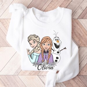 A white long-sleeved shirt with a graphic design featuring two cartoon girls and a snowman.