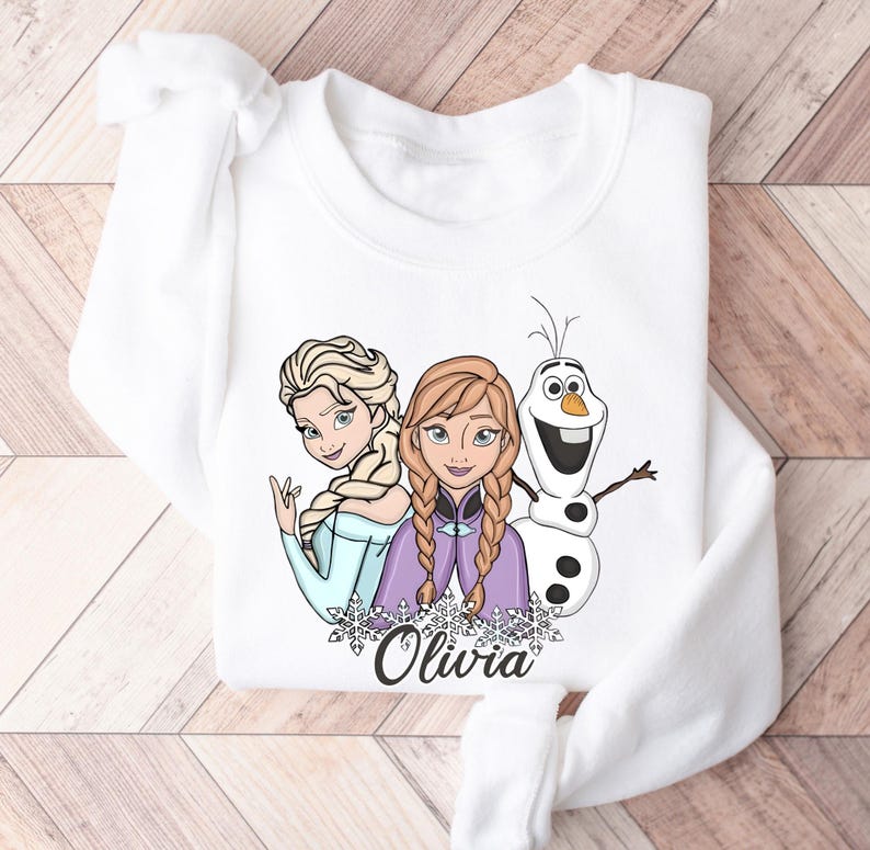 A white long-sleeved shirt with a graphic design featuring two cartoon girls and a snowman.