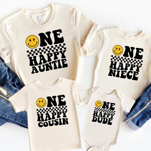 a collection of four white t-shirts with black text and a yellow smiley face design, arranged on a white background.