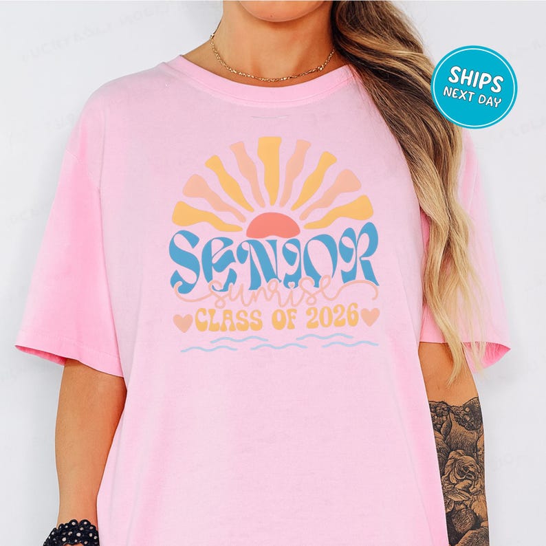 A woman wearing a pink t-shirt with a graphic design that says "SENIOR CLASS OF 2026" and features a sun-like design.