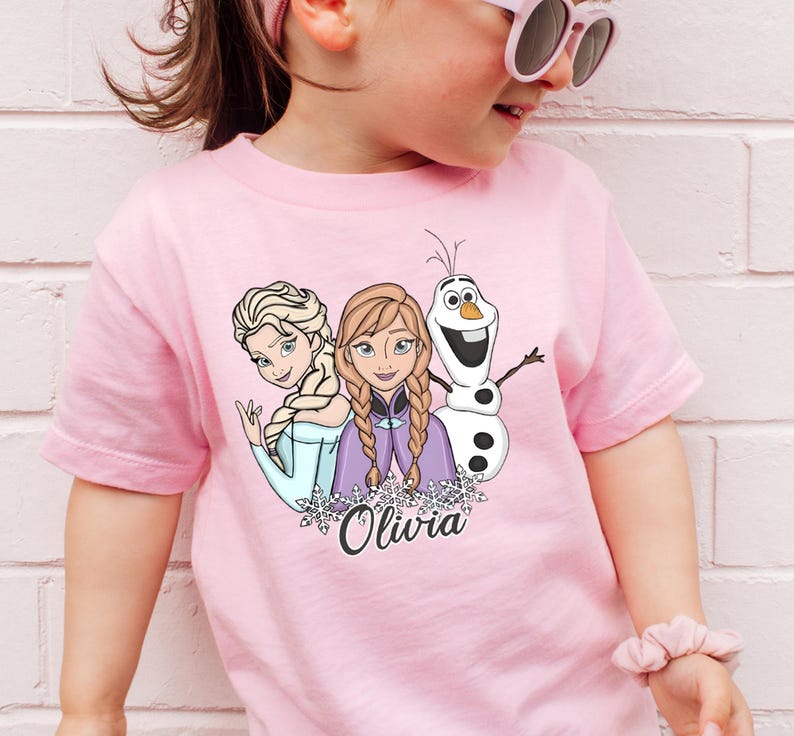 A young girl wearing a pink t-shirt with a graphic of the Disney characters Elsa, Olaf, and Oliva.