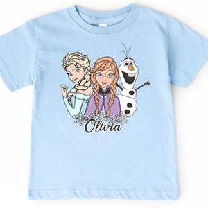 A light blue t-shirt with a graphic design featuring two cartoon girls and a snowman.