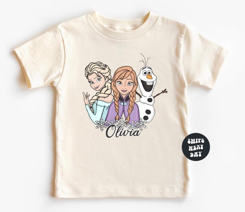 A white t-shirt with a graphic design featuring two cartoon characters, a girl and a snowman, along with the name "Olivia" written below them.