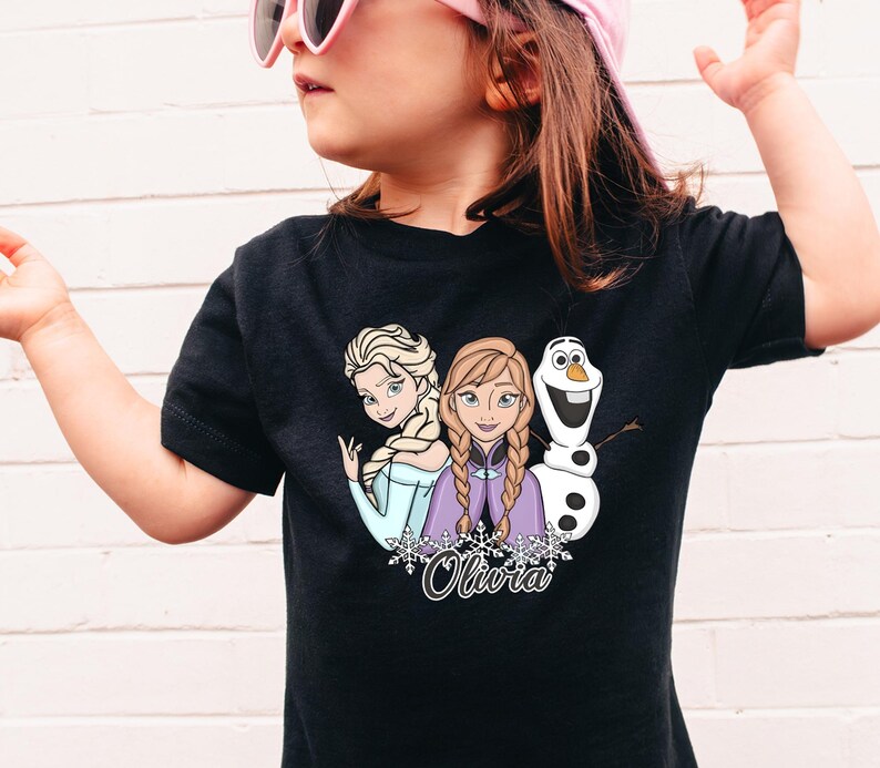 A young girl wearing a black t-shirt with a graphic of two cartoon characters, one of which is a snowman, and the other is a girl with blonde hair.