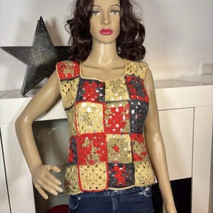 May include: A sleeveless crocheted vest with a patchwork design in red, beige, and black.