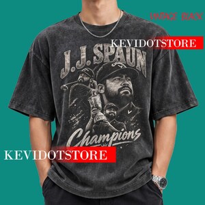 May include: A vintage black short-sleeve t-shirt featuring a graphic print of a golfer in a cap, holding a trophy, with the text J.J. SPAUN and Champions. The shirt has a distressed, washed-out appearance and a crew neckline.