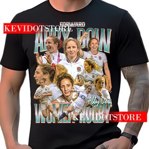 May include: Black t-shirt with a collage of images of a female rugby player. The name "Abby Dow" is in teal, with "Women's Rugby" below. The word "Forward" is above the name. The text "KEVIDOTSTORE" is in red.