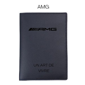 Pode incluir: Uma carteira de couro azul escuro com o logotipo AMG e o texto "UN ART DE VIVRE" impresso em branco. A carteira tem formato retangular e textura lisa. O logotipo AMG está localizado na parte superior.