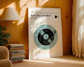 Könnte beinhalten: Ein weiß gerahmtes Poster mit dem Text "Let's play another and another" und einer Schwarzweißillustration eines Plattenspielers vor blauem Hintergrund. Das Poster hat ein kleines Blattsymbol und das Wort "feel" in der oberen rechten Ecke.