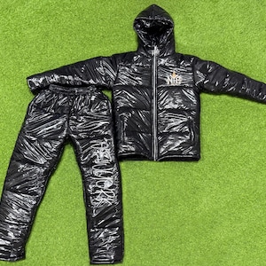 May include: Black puffer jacket and matching pants with a shiny finish. The jacket has a hood and a zipper closure. The pants have a drawstring waistband. Both pieces feature a white logo with the text "NEW YORK".