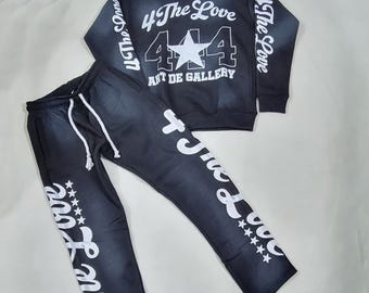 May include: A black hoodie and matching sweatpants set. The hoodie features the text "4 The Love" and "444 ART DE GALLERY" in white. The sweatpants have the text "4 The Love" in white. The set is made of a dark denim-like material.
